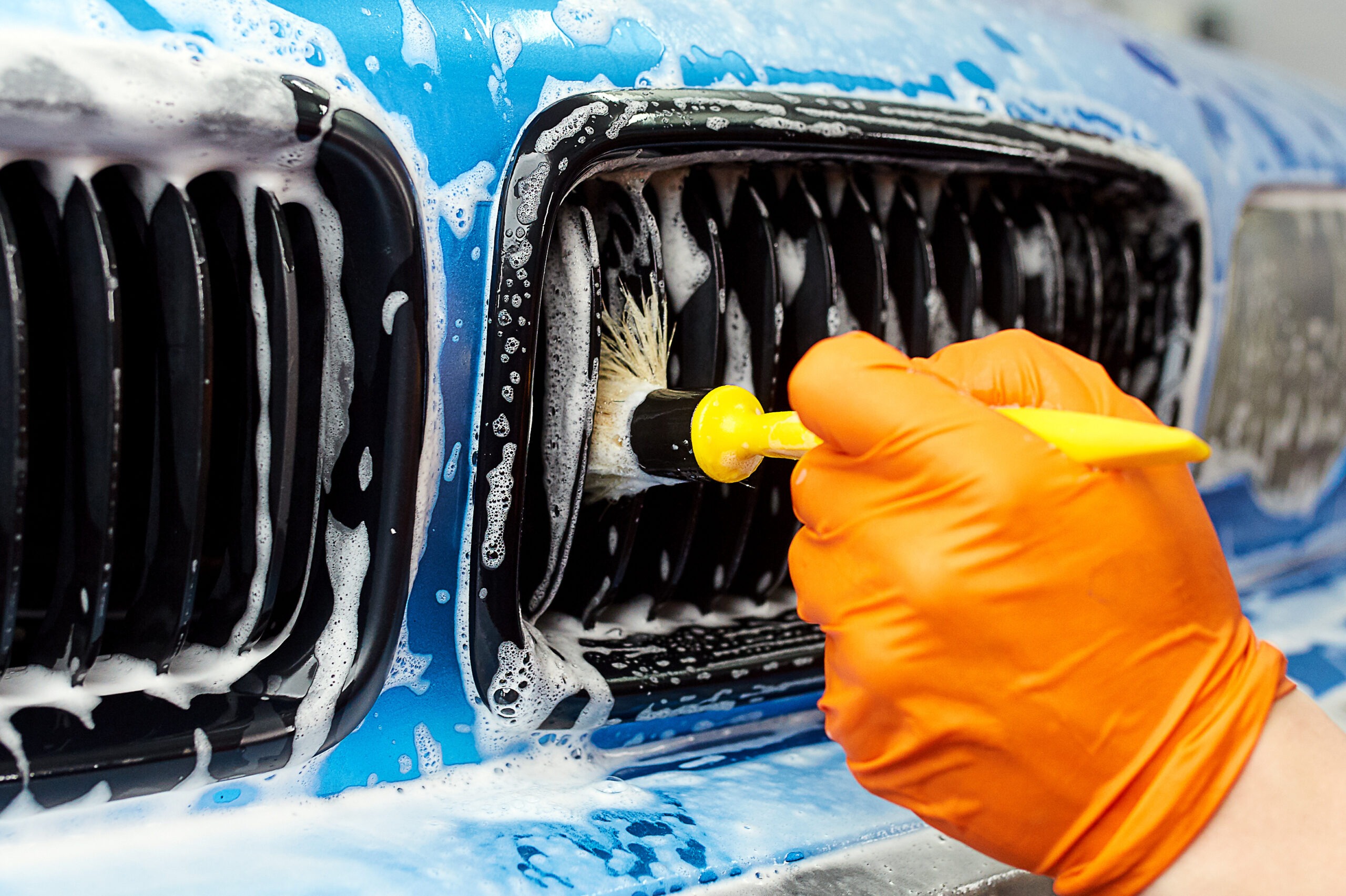 detailed car wash Detailer using a brush to clean the slats of a car grill during an exterior auto detailing service