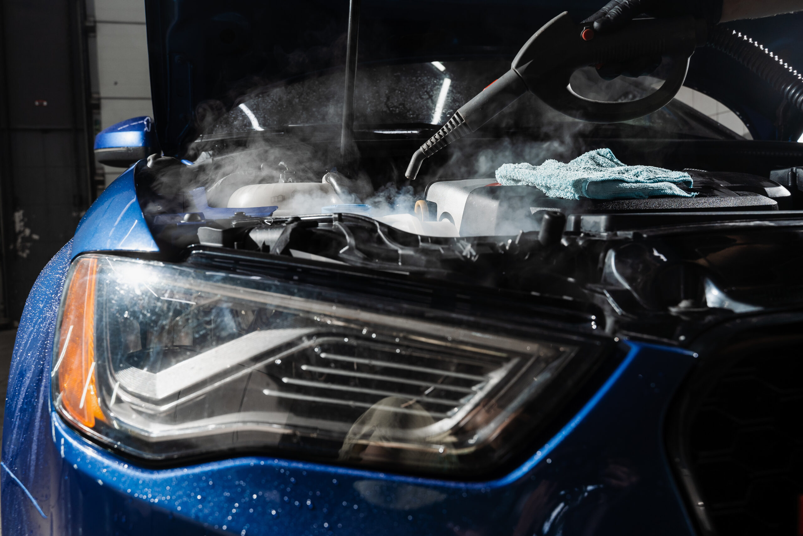 Steaming washing of motor of auto in detailing auto service. Process of steam cleaning car engine from dust and dirt. Steam washing a car engine to remove dust and dirt during a professional detailing service